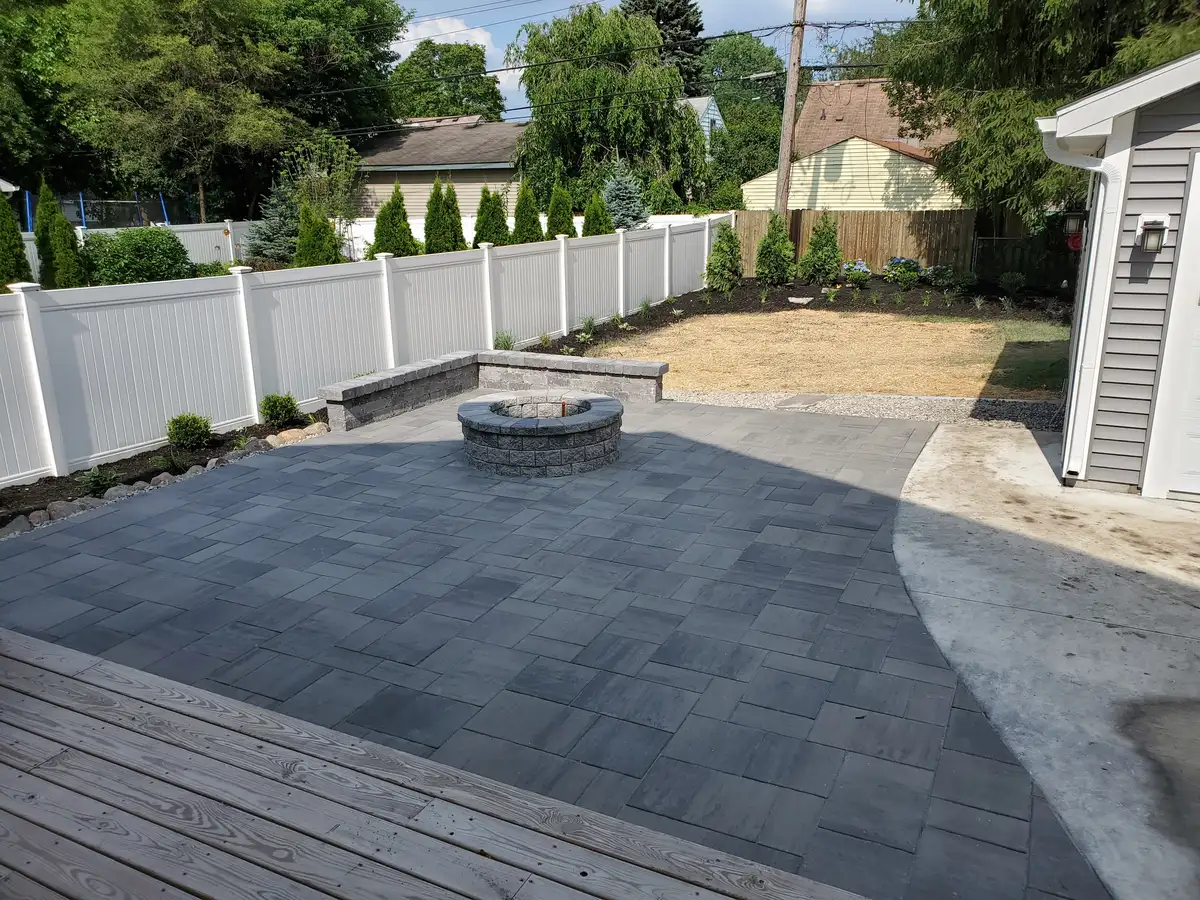 Paver patio with built-in fire pit and seat wall in fenced Metro Detroit backyard by The Guy Outdoor Services