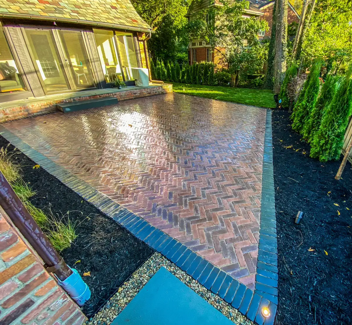 Finished brick patio bordered by dark mulch beds and evergreen plantings