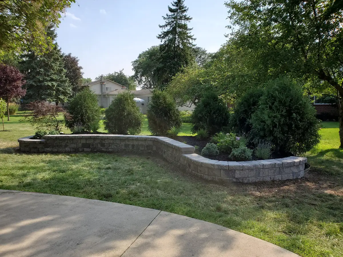 Curved segmental block retaining wall with capstone in landscaped backyard by The Guy Outdoor Services