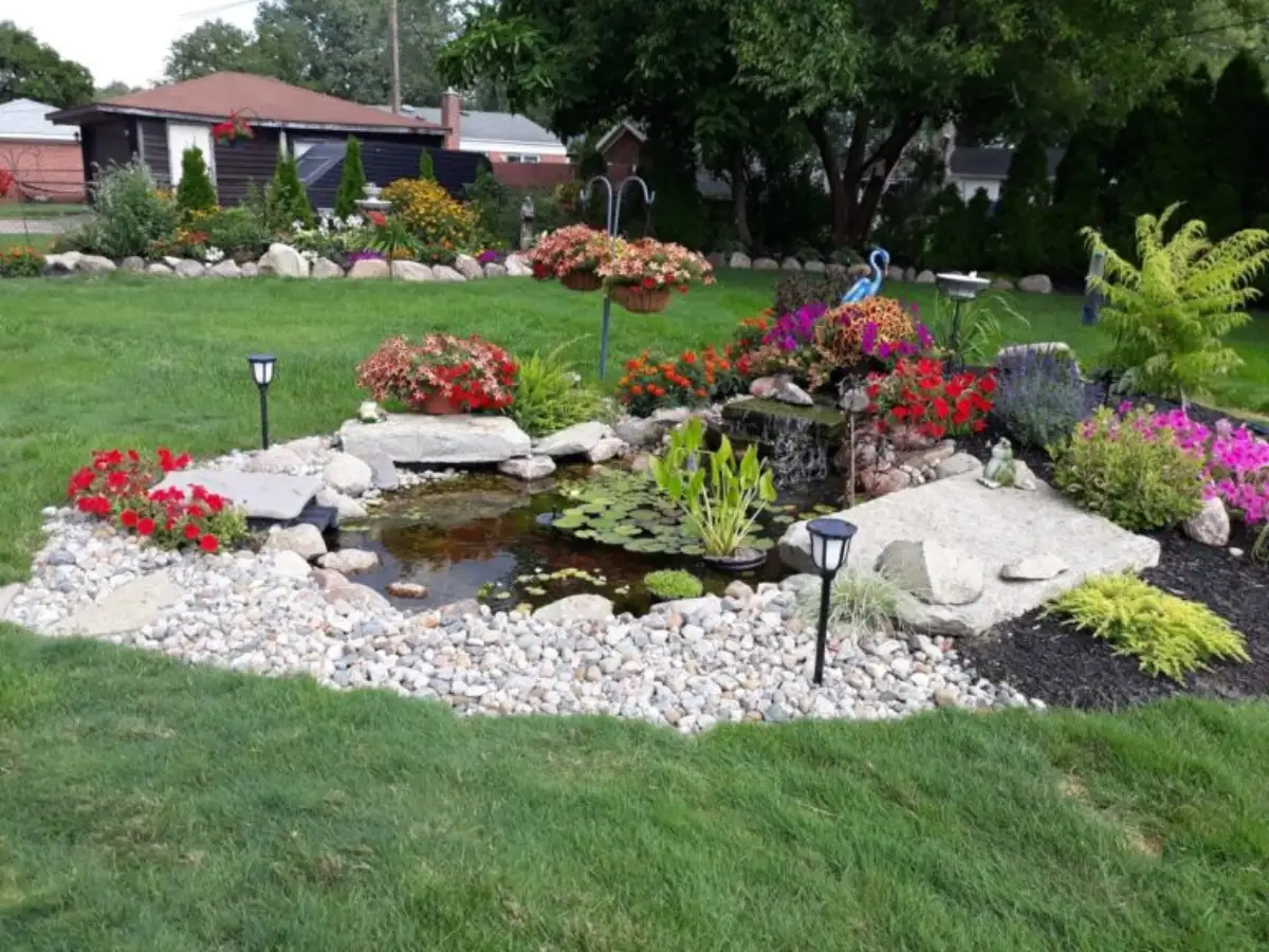 Colorful garden pond with cascading waterfall, lily pads, and flowering plants by The Guy Outdoor Services